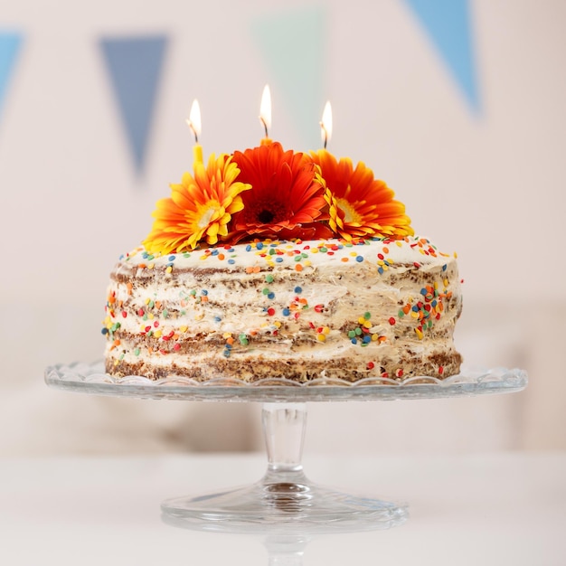 Primo piano di una deliziosa torta di compleanno crema fatta in casa bianca decorata con fiori freschi e candele