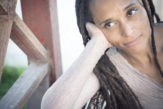 Primo piano di una donna afroamericana con una lunga acconciatura intrecciata che riposa il viso sul palmo della mano e distoglie lo sguardo all'aperto. Donna premurosa con i capelli intrecciati che guarda lontano