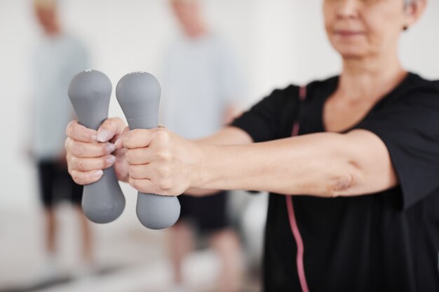 Primo piano di una donna anziana che allunga le braccia con i manubri mentre fa esercizi in palestra