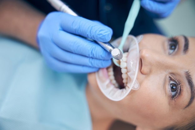 Primo piano di una donna attraente sdraiata su una sedia mentre un professionista maschio le sta perforando i denti