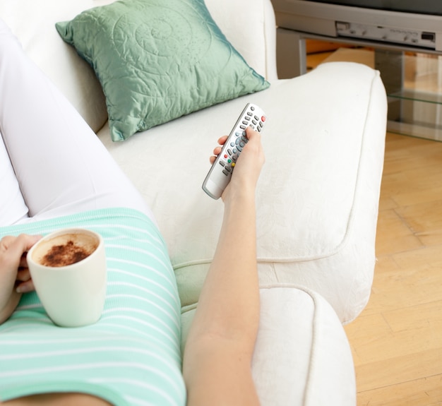 Primo piano di una donna che beve un caffè mentre si guarda la TV