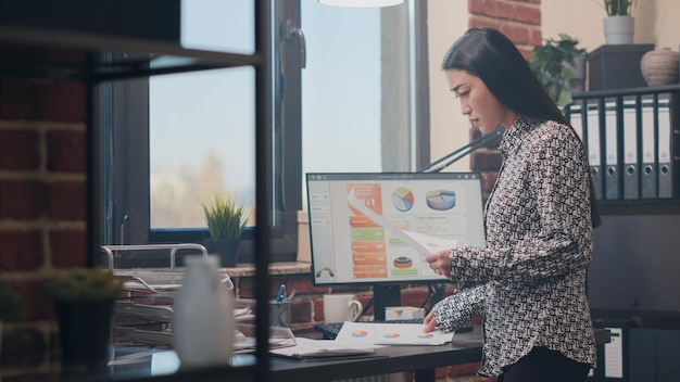 Primo piano di una donna che confronta i dati sui documenti con il computer per lavorare sulla strategia aziendale. Imprenditore che utilizza i documenti per pianificare il progetto finanziario per lo sviluppo nel lavoro di una società di avvio.