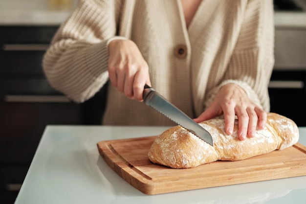 Primo piano di una donna che taglia il pane su un tagliere di legno