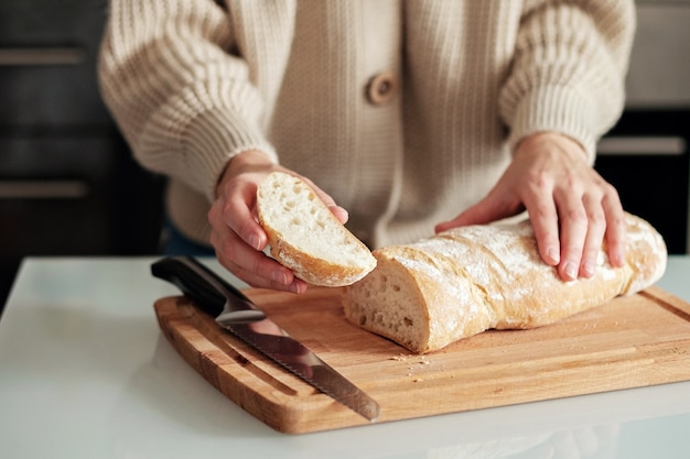 Primo piano di una donna che taglia il pane su un tagliere di legno