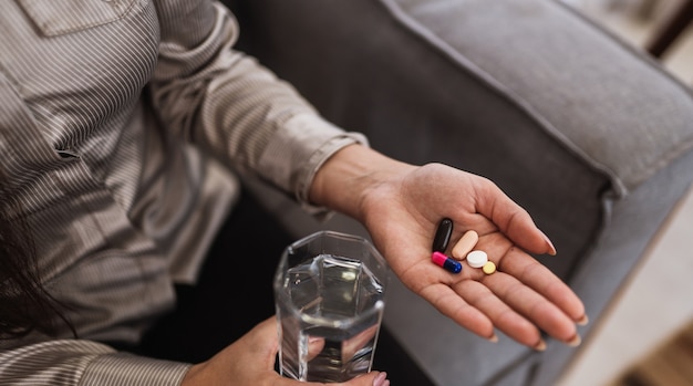 Primo piano di una donna che tiene in mano varie compresse, pillole e bicchiere d'acqua.