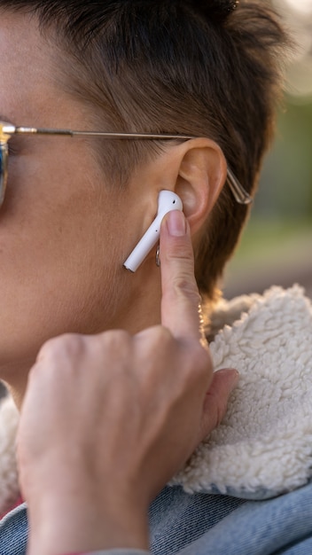 Primo piano di una donna che utilizza a mano auricolari true wireless bianchi per metterli nell'orecchio e controllarli