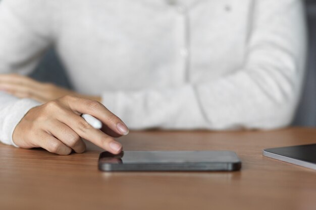 Primo piano di una donna che utilizza smartphone e tiene in mano una penna stilo su un tavolo di legno con abiti casual