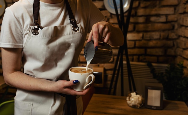 Primo piano di una donna che versa la crema in una tazza di caffè nella cucina di un bar-caffetteria o di un ristorante. barista