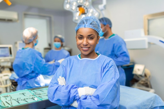 Primo piano di una donna chirurgo afroamericano guardando la fotocamera con i colleghi che si esibiscono in background in sala operatoria Il concetto di medicina