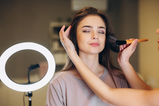 Primo piano di una donna con i capelli castani che si trucca. Pennello da trucco vicino al viso.