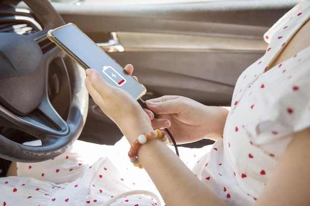 Primo piano di una donna con un vestito bianco che carica il suo telefono cellulare con il cavo di ricarica per auto