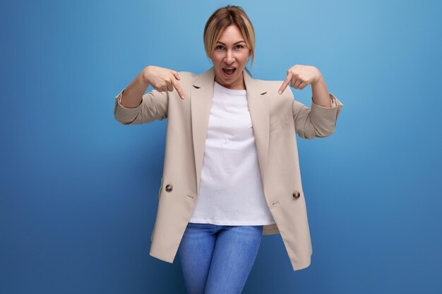 Primo piano di una donna d'affari bionda in una giacca che punta il dito su uno sfondo blu con copia