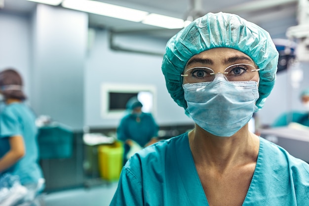 Primo piano di una donna del chirurgo con i colleghi che eseguono nella stanza in funzione del fondo.