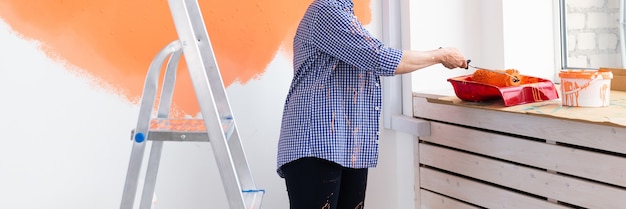 Primo piano di una donna di mezza età che dipinge il muro con un rullo di vernice. Ritratto di una giovane bella donna che dipinge il muro nel suo nuovo appartamento. Concetto di ristrutturazione e ristrutturazione.