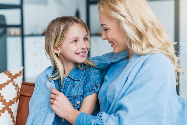 Primo piano di una donna felice che si lega a sua figlia mentre è seduta sul divano sotto la coperta