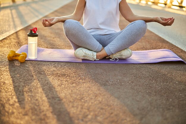 Primo piano di una donna in abiti sportivi seduta nella posizione del loto e che fa esercizi di meditazione yoga all'aperto