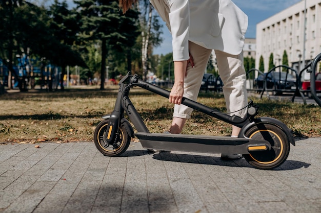 Primo piano di una donna in abito bianco che piega il suo scooter elettrico dopo il giro mentre si trova in un parco cittadino