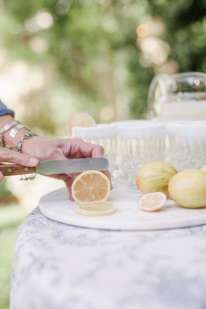 Primo piano di una donna in piedi a un tavolo in un giardino che affetta i limoni per un drink