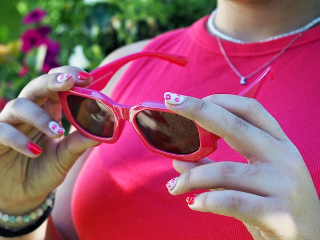 Primo piano di una donna in una camicia rosa che tiene gli occhiali da sole in mano con la manicure