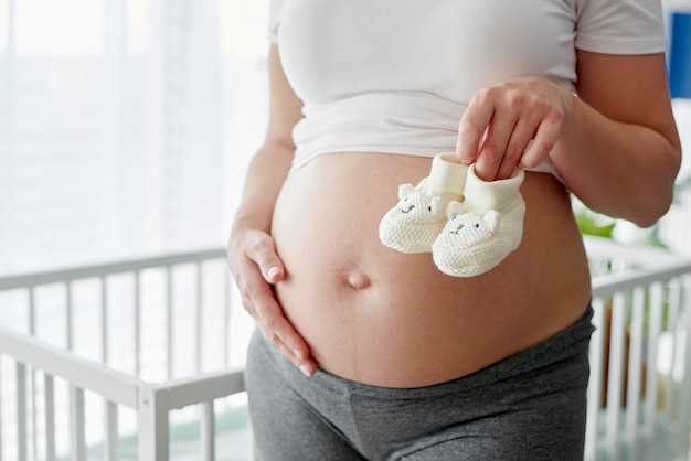 Primo piano di una donna incinta che tiene in mano un paio di scarpe per bambini