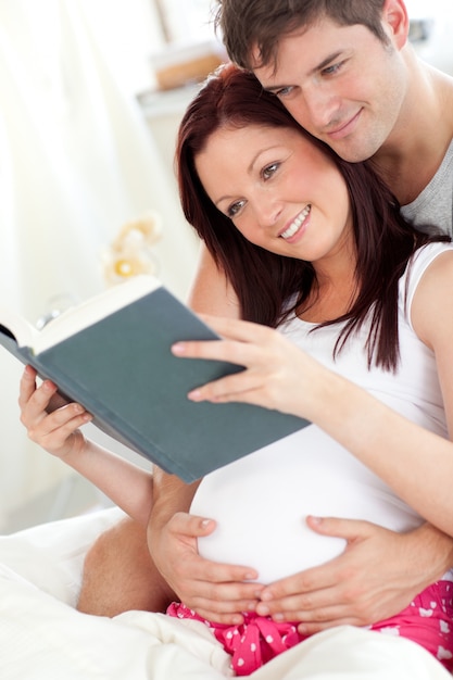 Primo piano di una donna incinta felice e suo marito leggendo un libro sul divano