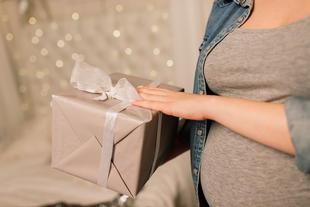 Primo piano di una donna incinta sorridente felice che si tocca la pancia sullo sfondo dell'albero di natale