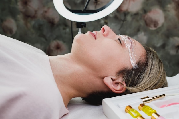 Primo piano di una donna matura che ottiene la procedura di laminazione delle sopracciglia presso il salone di bellezza.