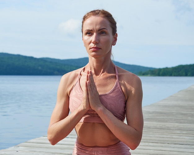 Primo piano di una donna matura in una tuta rosa che pratica yoga con le mani giunte con i palmi delle mani insieme