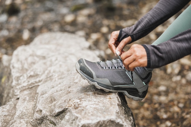 Primo piano di una donna nera irriconoscibile che lega le sue scarpe da ginnastica nella foresta durante le escursioni o il jogging sulla montagna.
