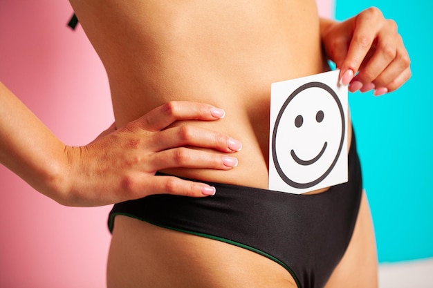 Primo piano di una donna sana con un bel corpo sottile in forma che tiene la carta con uno smiley felice