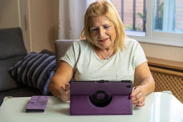 Primo piano di una donna sulla sessantina seduta a casa con il suo tablet e felice