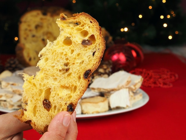 Primo piano di una fetta di panettone con frutta candita e uvetta che un uomo tiene in mano