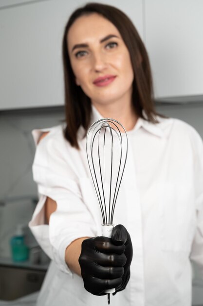 Primo piano di una frusta nelle mani di un pasticcere. Giovane pasticcere femminile con frusta.