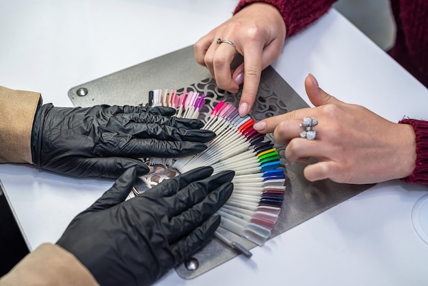 Primo piano di una giovane bruna che cerca di scegliere il colore giusto di smalto per unghie in un salone di bellezza Concetto di lavoro di salone di bellezza per le donne