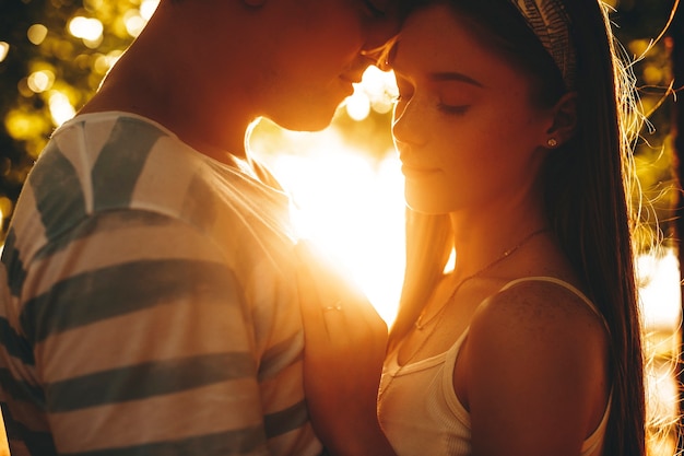 Primo piano di una giovane coppia con la testa che tocca contro il tramonto. Uomo e donna che si abbracciano mentre si incontra all'aperto nel parco.