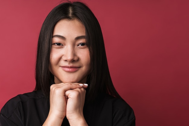 Primo piano di una giovane donna asiatica abbastanza sorridente che indossa abiti casual in piedi isolata sul muro rosso