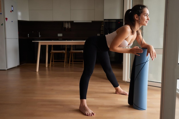 Primo piano di una giovane donna attraente che stende un tappetino da yoga o fitness blu prima di allenarsi in studio Stile di vita sano