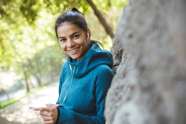 Primo piano di una giovane donna attraente fitness indossando abiti sportivi che esercitano all'aperto, ascoltando musica con gli auricolari