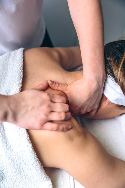 Primo piano di una giovane donna che riceve un massaggio sulle spalle in un centro clinico. Medicina, sanità e concetto di bellezza.