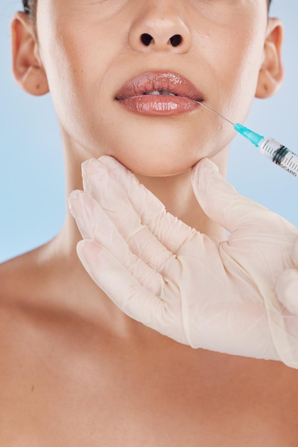 Primo piano di una giovane donna che riceve un trattamento di iniezione delle labbra da un medico cosmetico in uno studio Siringa e ago con riempitivo di botox per la bocca da un'estetista di cosmetologia con uno sfondo blu