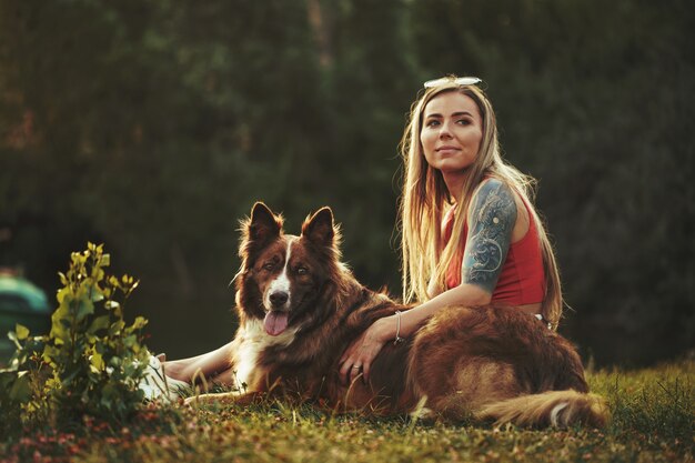 Primo piano di una giovane donna con il suo cane seduto sull'erba in park