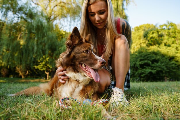 Primo piano di una giovane donna con il suo cane seduto sull'erba nel parco