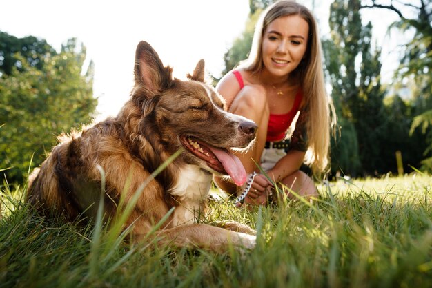 Primo piano di una giovane donna con il suo cane seduto sull'erba nel parco