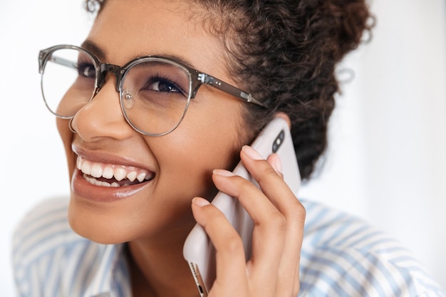 Primo piano di una giovane donna d'affari africana sorridente che parla al telefono cellulare al chiuso