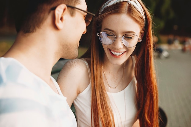 Primo piano di una giovane donna dai capelli rossi con le lentiggini che ride con gli occhi chiusi risalente al suo uomo. Bella coppia di incontri all'aperto e divertirsi.