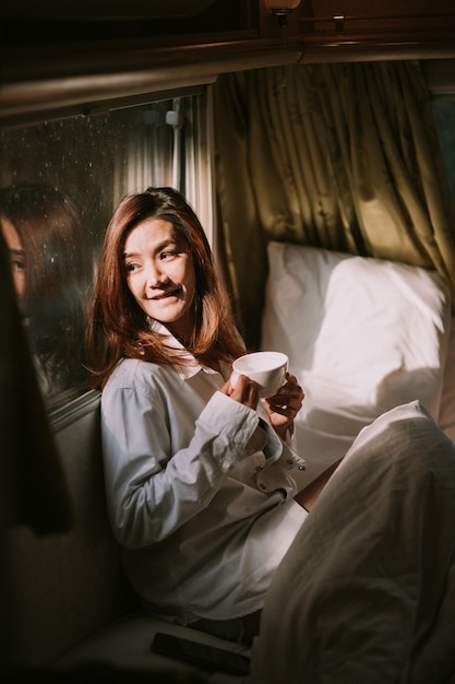 primo piano di una giovane donna felice con una tazza di caffè o una bevanda al cacao a letto?