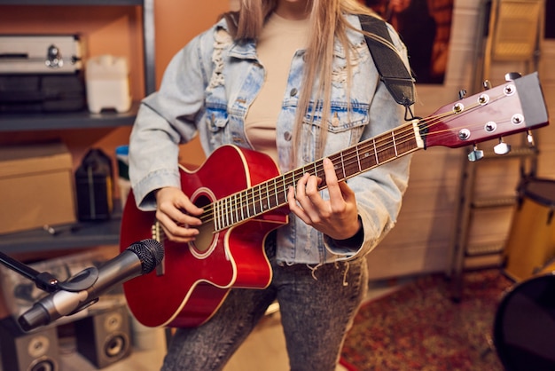 Primo piano di una giovane donna in piedi davanti al microfono e che suona la chitarra in studio di registrazione