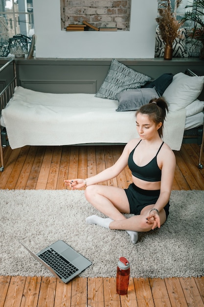Primo piano di una giovane donna in uniforme sportiva è appoggiato sul pavimento a casa, guarda un film e studia da un laptop