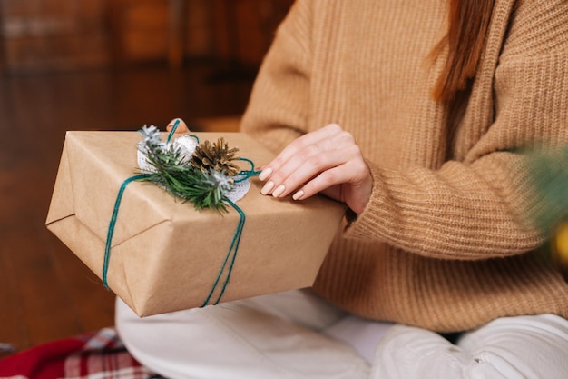 Primo piano di una giovane donna irriconoscibile che apre una scatola regalo di Natale con un regalo di Natale