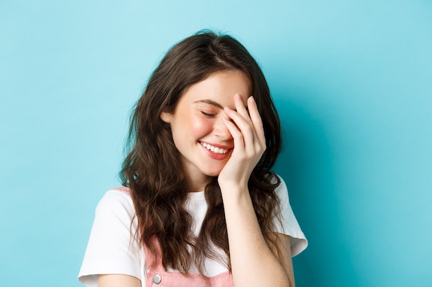 Primo piano di una giovane e bella donna che ride e arrossisce coprendosi il viso dietro la mano e sorridendo felice...